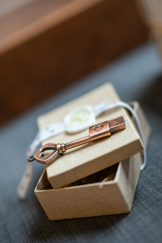 Clé USB enæ forme de clé avec une æfinition cuivrée, présentée dans une boîte en carton avec un ruban blanc et un sceau circulaire.